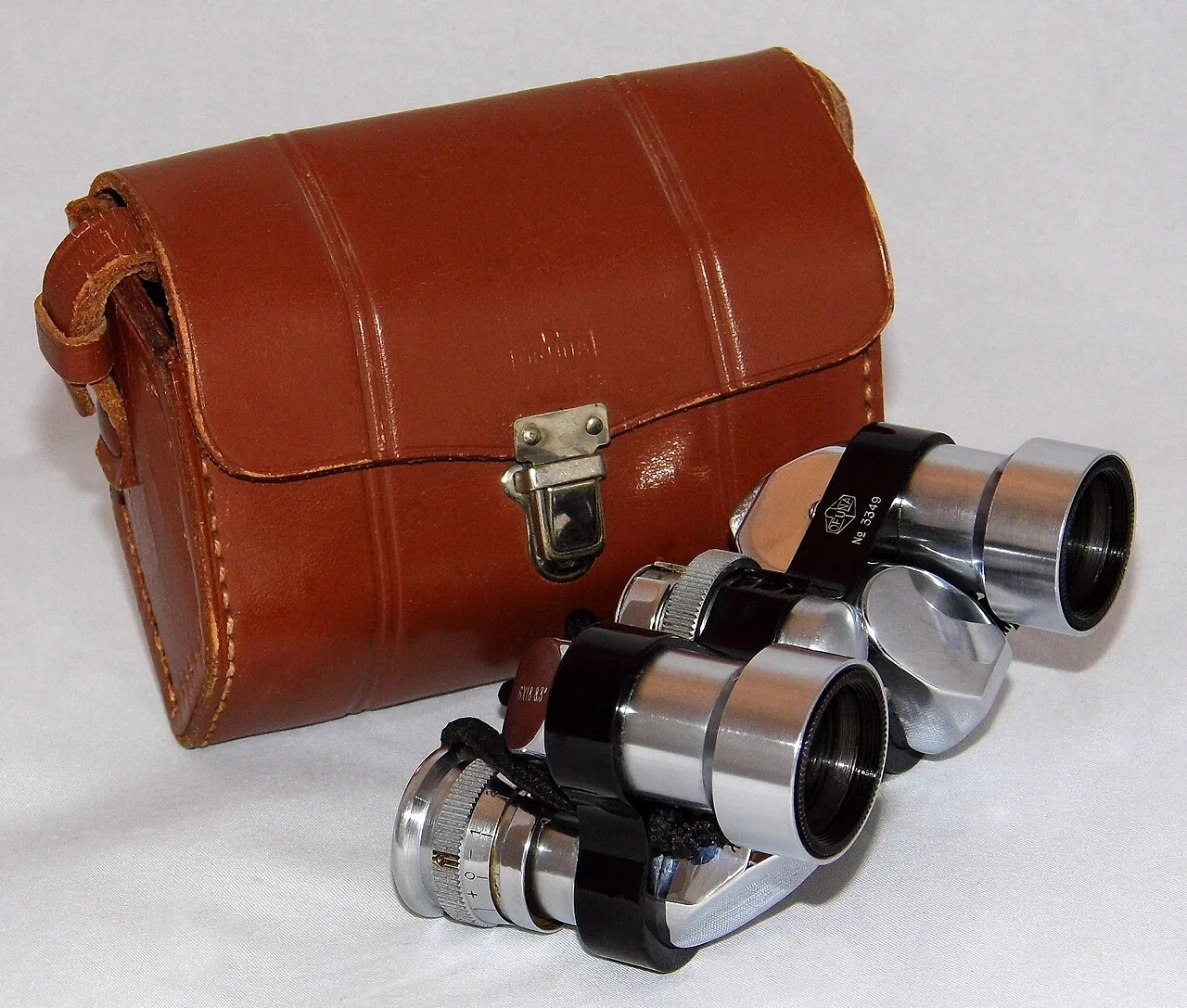 Vintage miniature reverse-Porro binoculars beside their brown leather case.